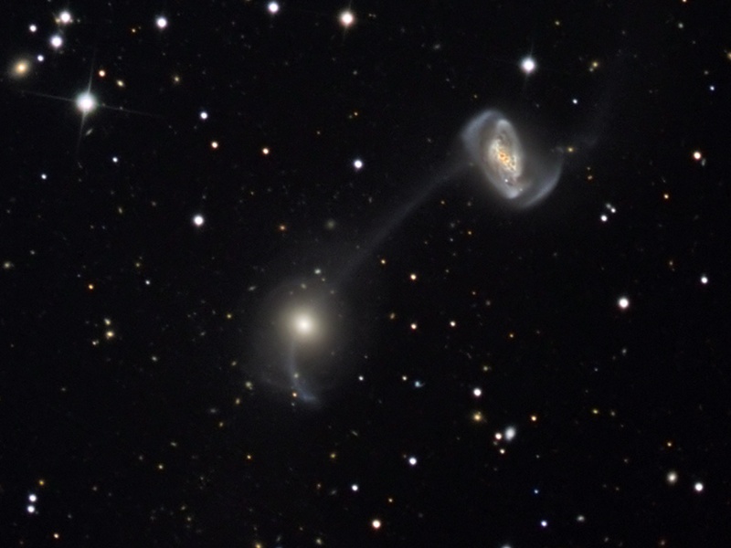 Zwei Galaxien fallen in diesem Bild auf: etwa in der Mitte eine verschwommene elliptische, und rechts oben eine Spiralgalaxie mit verzerrten Spiralarmen.