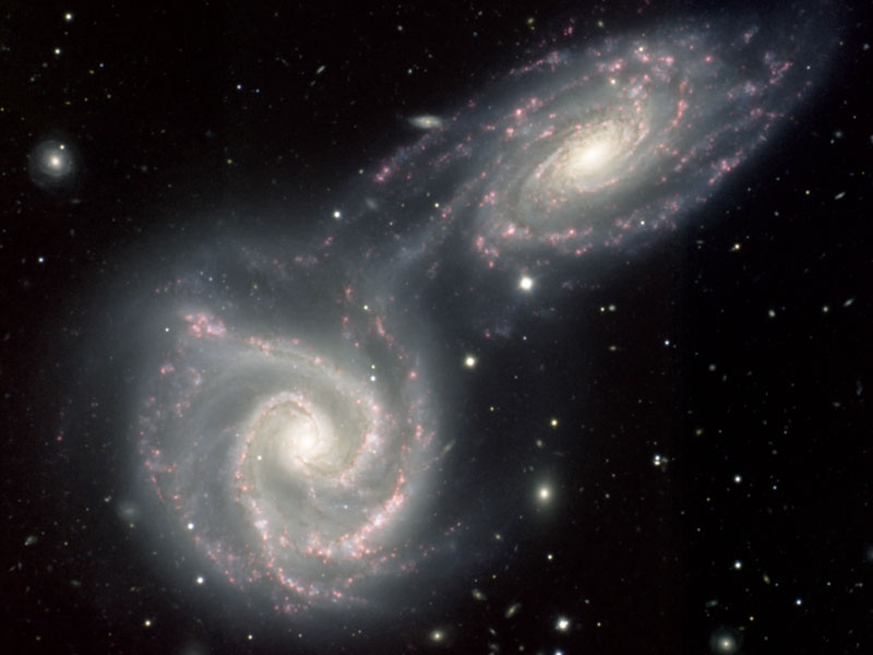 Am dunklen Hintergrund mit wenigen Galaxien leuchten zwei helle Spiralgalaxien. Links unten ist eine von oben sichtbare Spiralgalaxie, rechts oben eine leicht geneigte, beide sind auf Kollisionskurs.