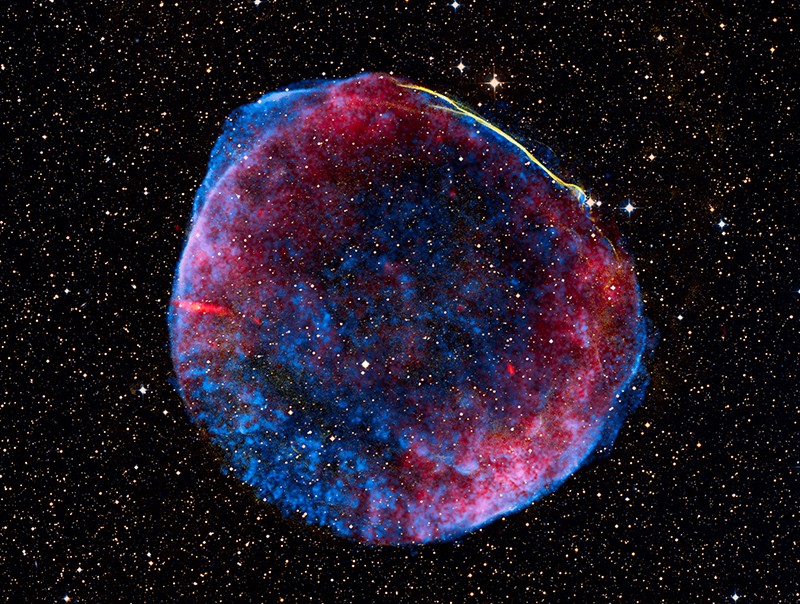 Vor einem dunklen Himmel mit Sternen leuchtet eine blau-rote Wolke, die eine optische Ähnlichkeit mit einer Seifenblase hat.