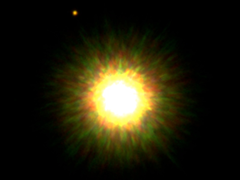 Das Bild zeigt einen hell leuchtenden Stern mit einem gelblichen Rand, der außen von grünlichen und orangefarbenen Lichtern umgeben ist.