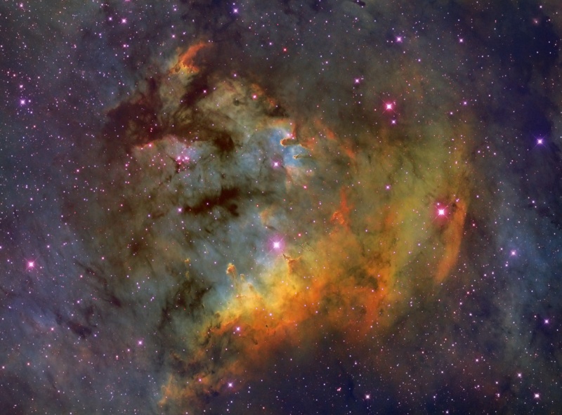 Das Bild zeigt einen farbigen Nebel vor einigen rot umrandeten Sternen.