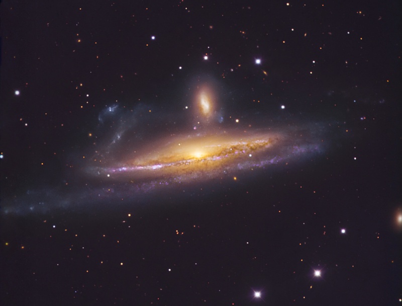 In der Mitte des Bildes mit nur wenigen Sternen leuchtet eine waagrechte Galaxie, die fast von der Seite sichtbar ist. Daüber ist eine viel kleinere senkrechte Galaxie abgebildet.