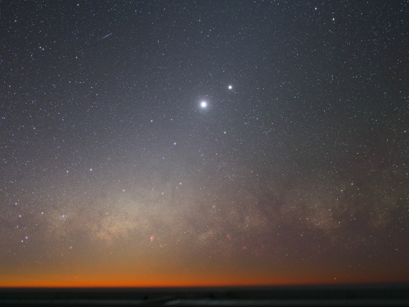 Über dem Horizont unten verläuft ein roter Streifen, am sternklaren Himmel darüber leuchten zwei helle Himmelslichter, die Planeten Venus und Jupiter.