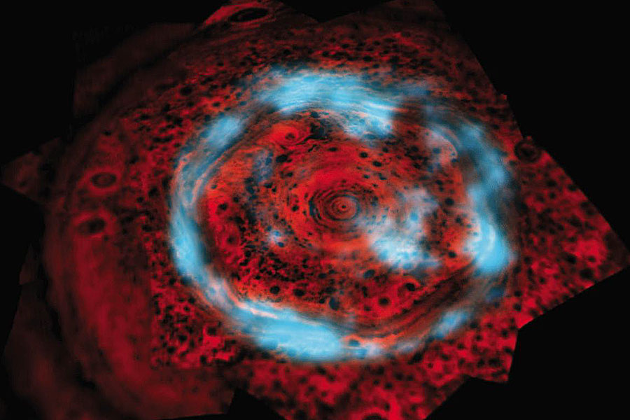 Der Bereich um den Nordpol des Saturn leuchtet rötlich aus dem dunklen Bild, darüber verlaufen hellblaue Wolken im Kreis. In den roten Wolken ist das Wolkensechseck erkennbar.