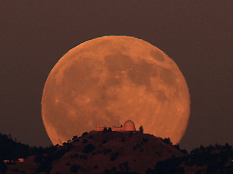 Hinter dem Lick-Observatorium auf einem Berg geht ein orangefarbenen Mond auf.