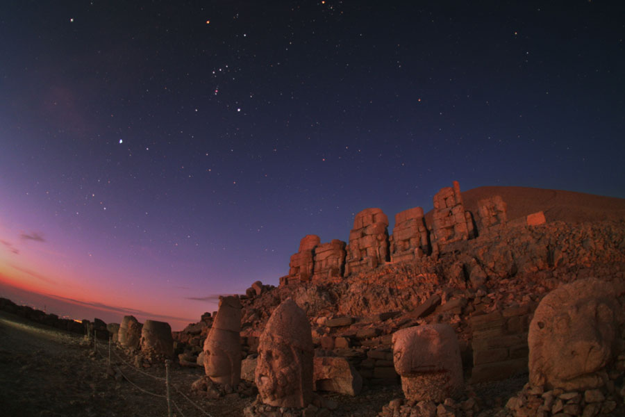 Hinter einer historischen Stätte mit gewaltigen Skulpturen leuchtet am Abendhimmel das Sternbild Orion.