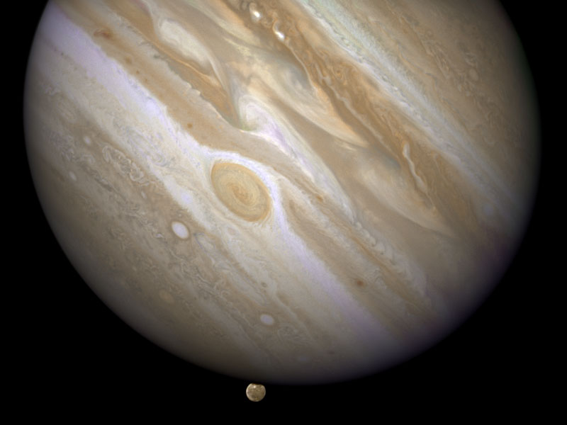 Jupiter ist diagonal und oben angeschnitten abgebildet, am unteren dunklen Rand ragt der Mond Ganymed hervor.