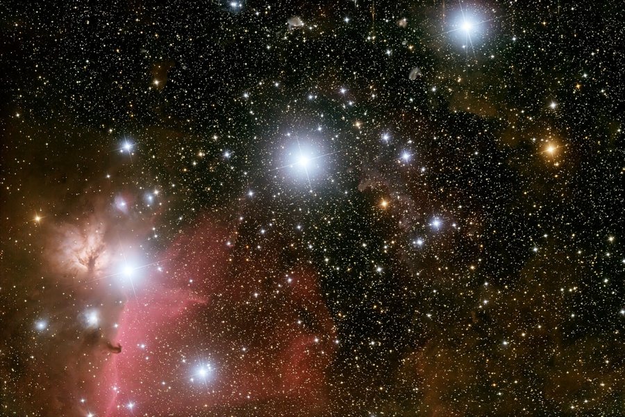 Das Bild zeigt die Gürtelsterne des Orion diagonal angeordnet, links unten leuchtet der Flammennebel, der Pferdekopfnebel zeichnet sich als Silhouette vor einem rötlichen Nebel ab.