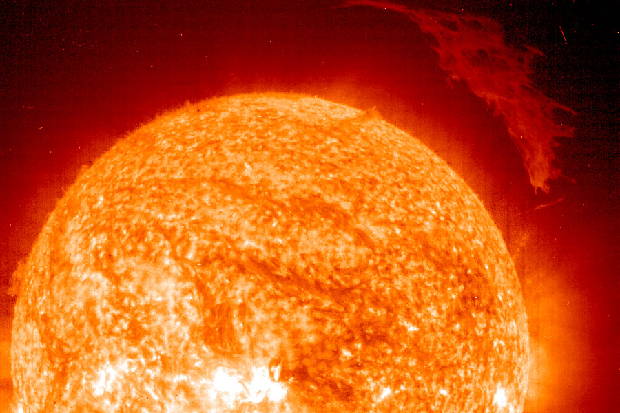 Links unten sind etwa drei Viertel der Sonne in leuchtend orangen und roten Farbtönen zu sehen, außern ist die Sonne von einem roten Nebel umgeben, und in der rechten oberen Ecke schwebt eine gewaltige Sonnenprotuberanz.