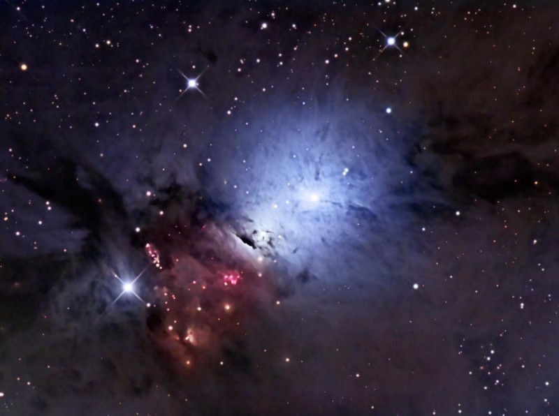 Um einen hellen Lichtfleck leuchtet ein blauer, wolkenartiger Nebel, nach links unten breitet sich ein dunkler Nebel mit roten Sternen darin aus.