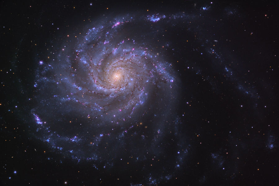 Die Galaxie links im Bild wirkt lilabläulich mit einem gelblichen Kern, ihre Spiralarme sind zerfledert und wirken lose.