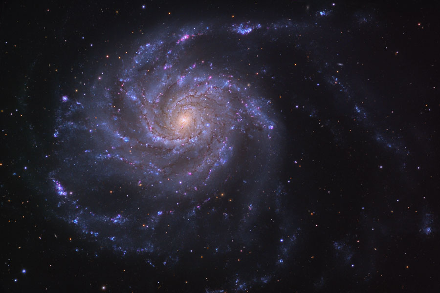 Die Galaxie links im Bild wirkt lilabläulich mit einem gelblichen Kern, ihre Spiralarme sind zerfledert und wirken lose.