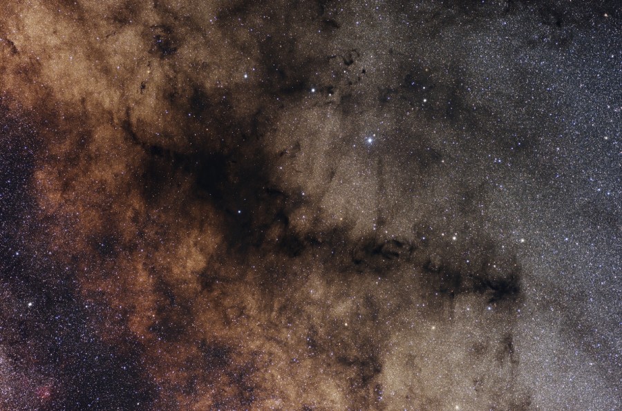 Das sterngefüllte Bild ist von markanten dunklen Staubwolken durchzogen.