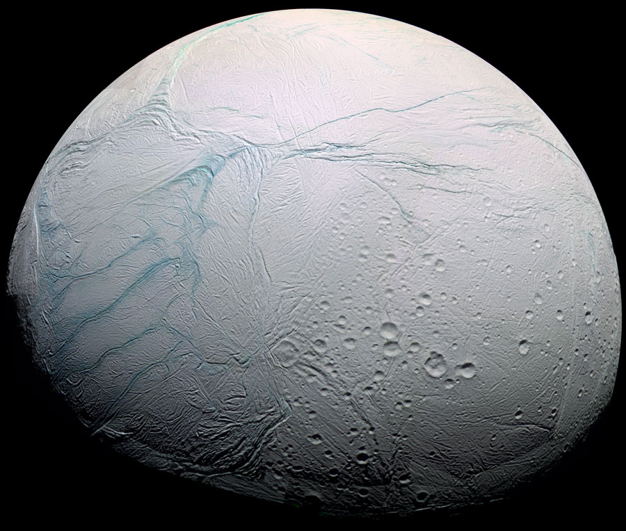 Der weiße Eismond Enceladus ist von oben fast ganz beleuchtet. Unten sind Krater erkennbar, oben verlaufen bläuliche Gräben durchs Eis.