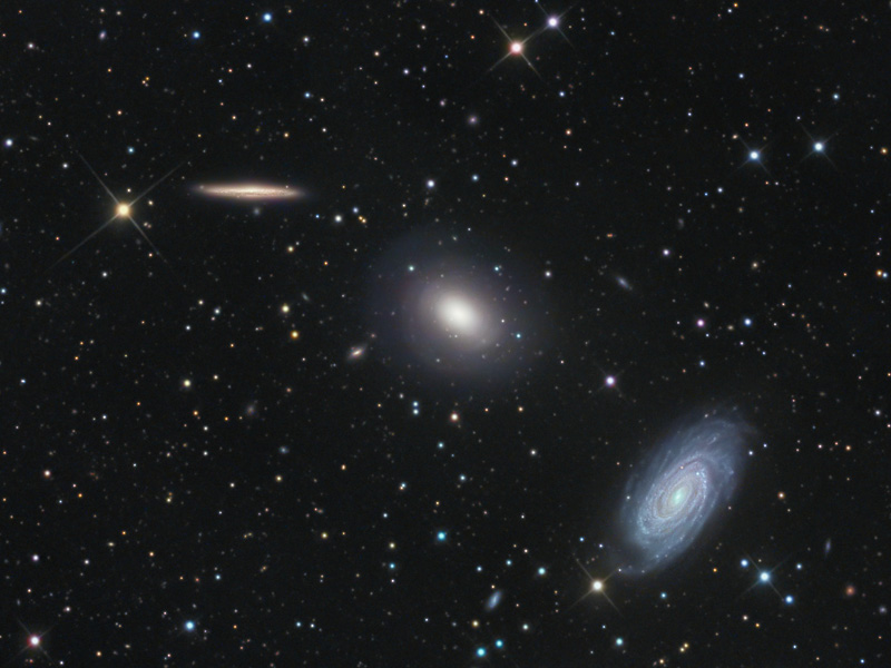 Im Bild sind diagonal von links oben nach rechts unten drei Galaxien angeordnet, die obere sehen wir von der Kante, die mittlere ist verschwommen, die untere ist halb geneigt und hat ausgeprägte Spiralarme.