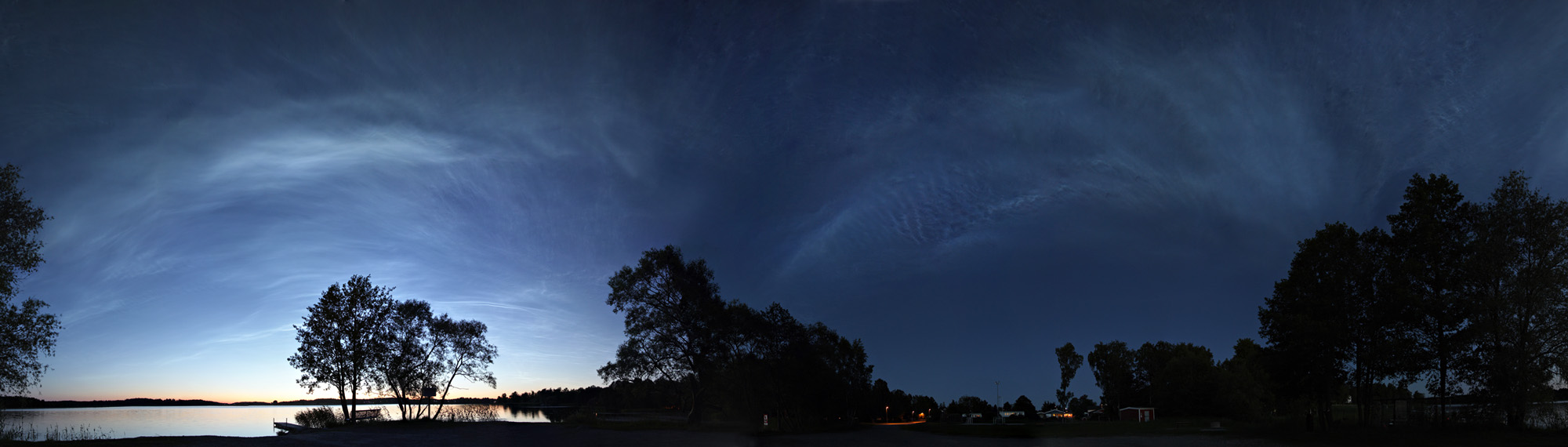 Links im Bild ist steht eine Baumgruppe, dahinter leuchten Nachtwolken. Der rechte Bildteil ist dunkel.