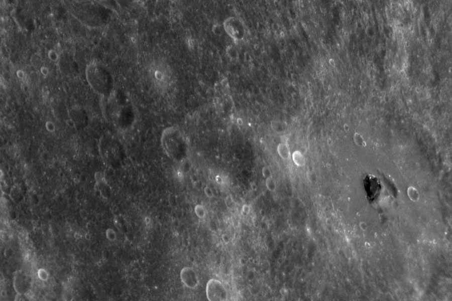 Die graue Oberfläche Merkurs ist von Kratern übersät, rechts ist ein dunkler Brocken erkennbar.