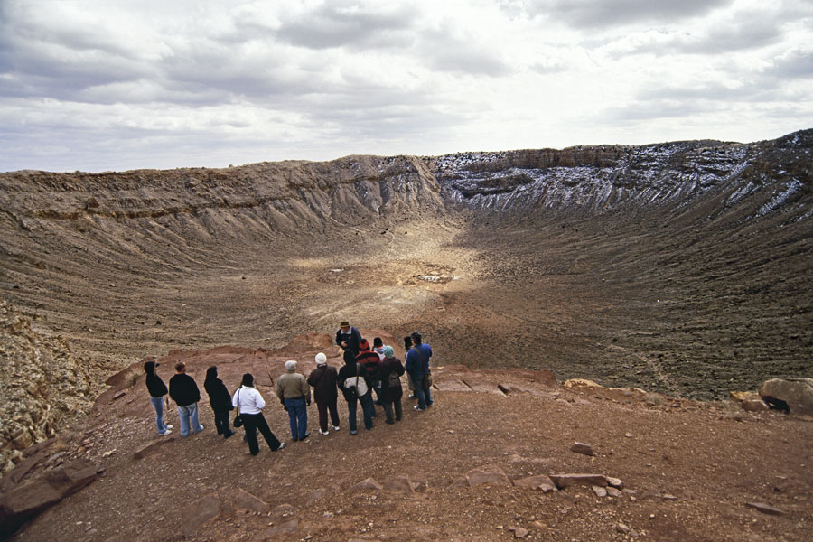 Eine Gruppe Menschen steht am Rand eines riesigen kahlen Kraters.