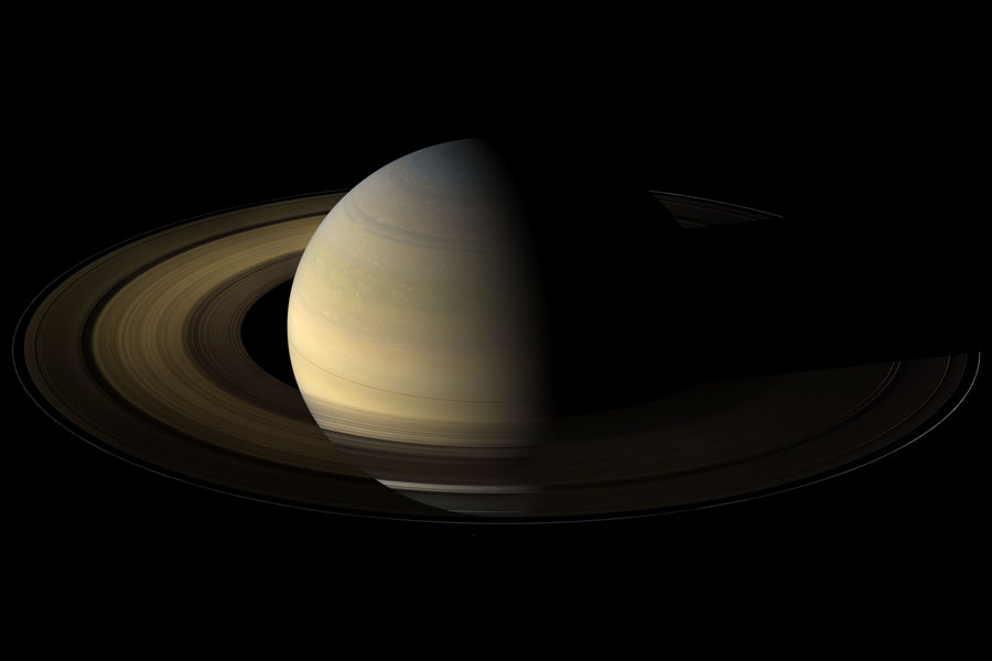 Der Planet Saturn und seine Ringe sind links zur Hälfte beleuchtet. Man sieht ihn schräg von oben.