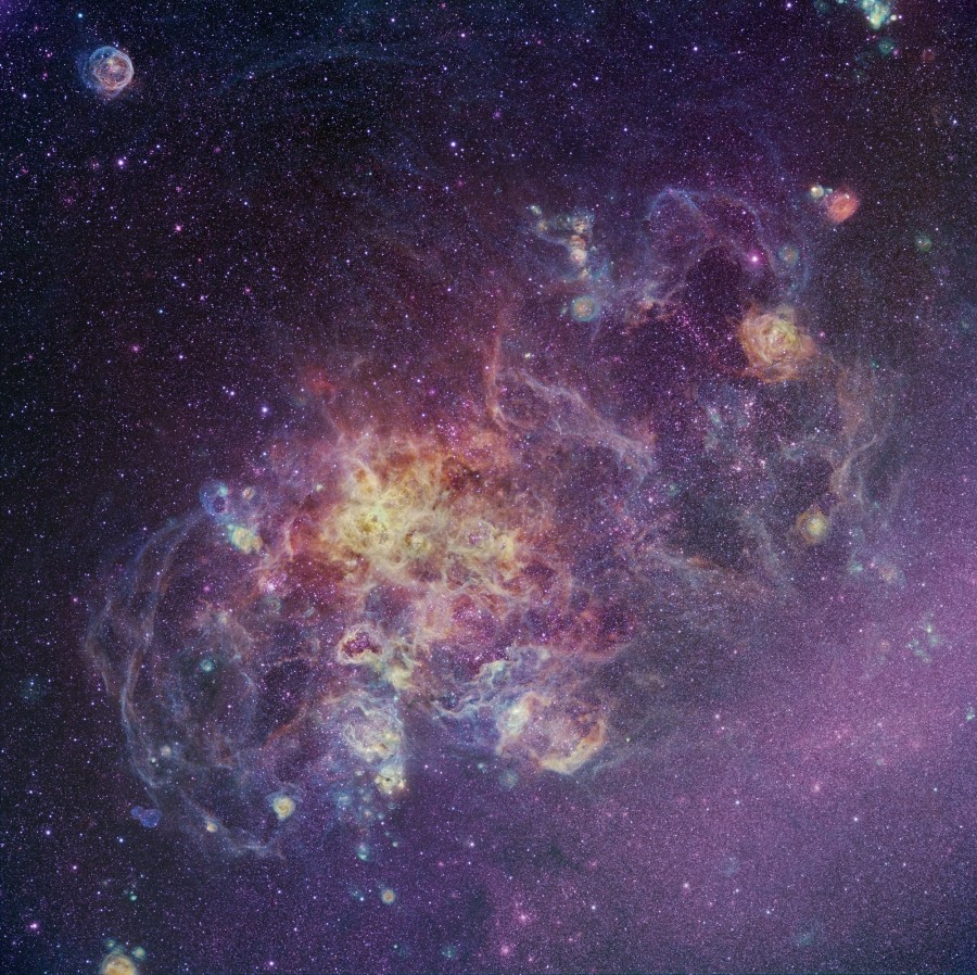Vor einem von Sternen bedeckten dunklen Hintergrund zeichnen sich verschlungene violette Nebel ab, die ein gelbes Zentrum besitzen.