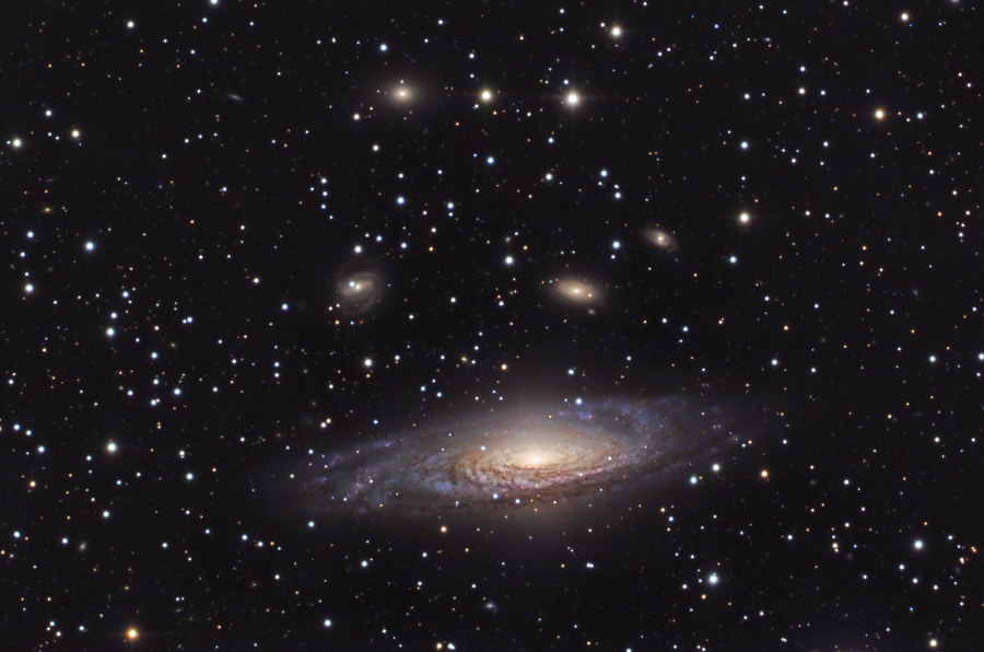 Hinter einem von Sternen gesprenkelten Vordergrund leuchtet eine große, schräg abgebildete Spiralgalaxie sowie im Hintergrund weitere Galaxien.
