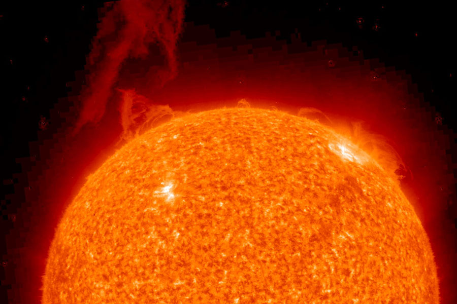 Die Sonne ist zur Hälfte dargestellt, sie ist orange und rot gefleckt mit einigen weißen Flecken. Oben ist eine rötliche Struktur hochgeschleudert.