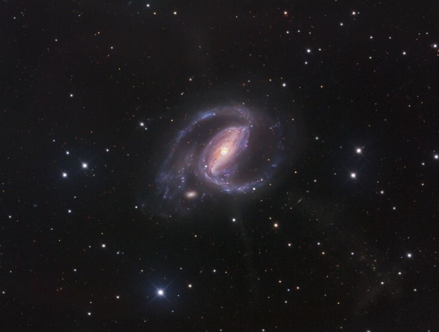 Mitten im Bild und von wenigen Sternen umgeben ist eine Galaxie mit sehr markantem Zentralbalken und zwei Spiralarmen.