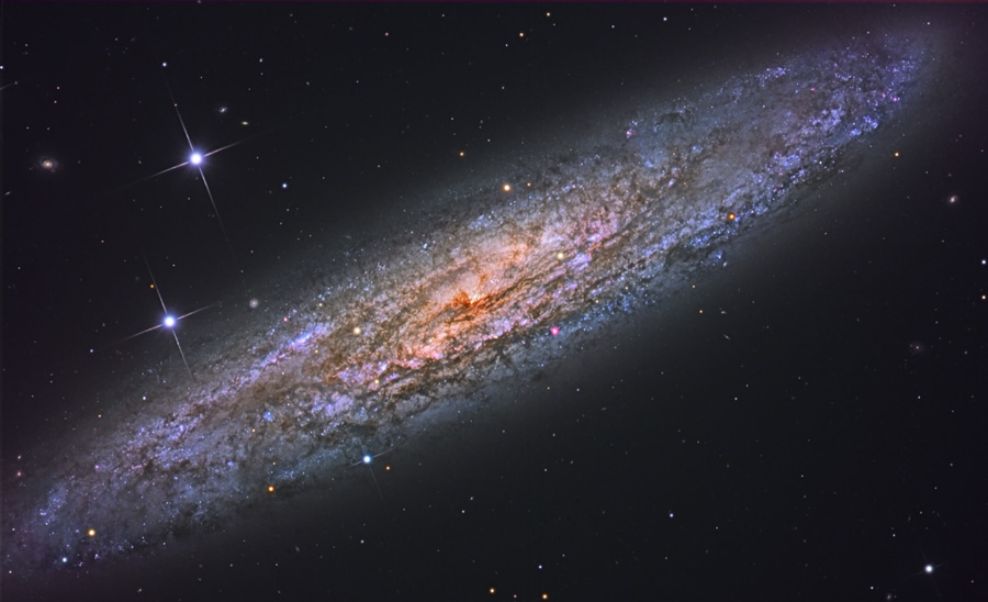 Im Bild ist diagonal eine Galaxie mit vielen dunklen Flecken abgebildet, sie ist von schräg oben zu sehen.