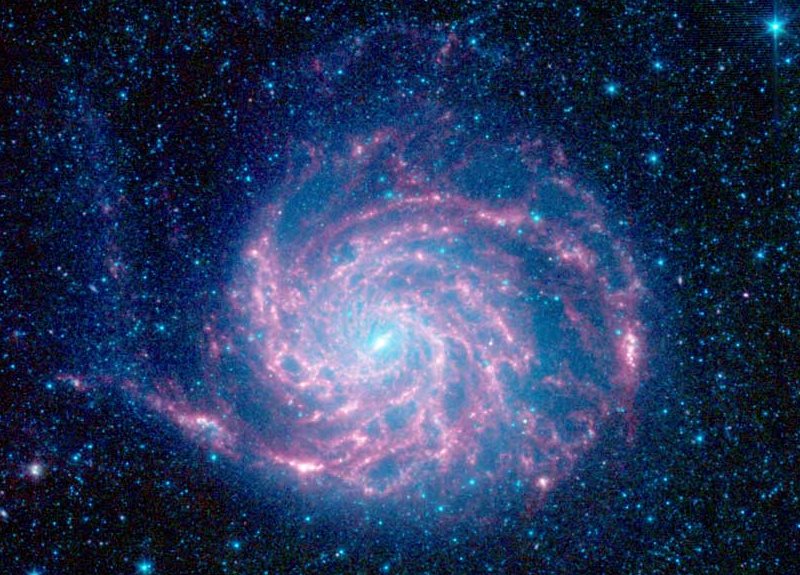 Im Bild rotiert eine Galaxie mit rosaroten Spiralarmen, darum herum sind blau gefärbte Sterne verteilt.