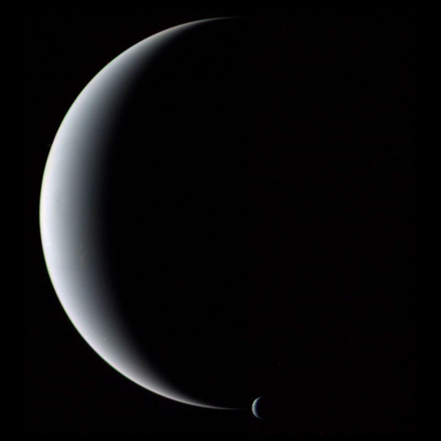 Zwei sehr glatte, matt beleuchtete Kugeln sind als Sicheln zu sehen,
links der große Neptun und an der unteren Spitze die kleine Sichel des Mondes Triton.