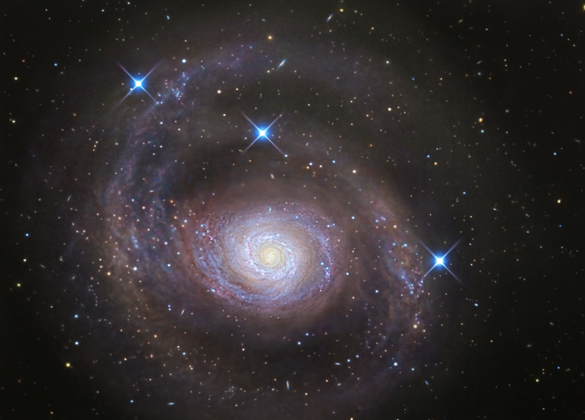 Die Galaxie im Bild ist in der Mitte hell mit vielen blauen Sternbildungsregionen, von dort aus verlaufen zuerst eng gewundene Spiralarme, die nach außen hin immer weiter werden.