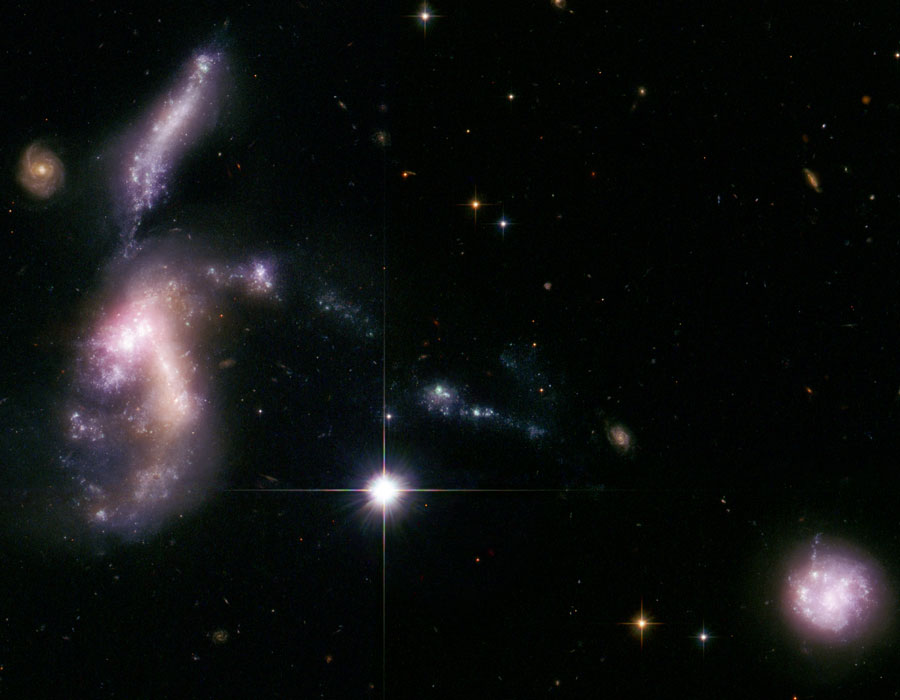 Links sind zwei größere unregeläßige Galaxien und eine kleinere, regelmäßige Spiralgalaxie, rechts unten eine kleine, helle Galaxie, und unter der Mitteleuchtet ein Stern.