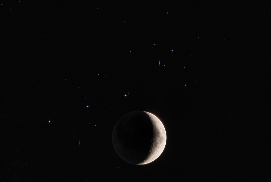 Unten in der Mitte leuchtet eine breite Mondsichel, darüber sind die blassen Sterne der Plejaden verteilt.