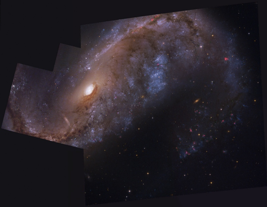 Zwischen dunklen Blenden ragt eine gewaltige Galaxie auf, in der Mitte leuchtet ein helles kleines Zentrum, darum herum sind Wolken mit Sternbildung zu Spiralarmen angeordnet.