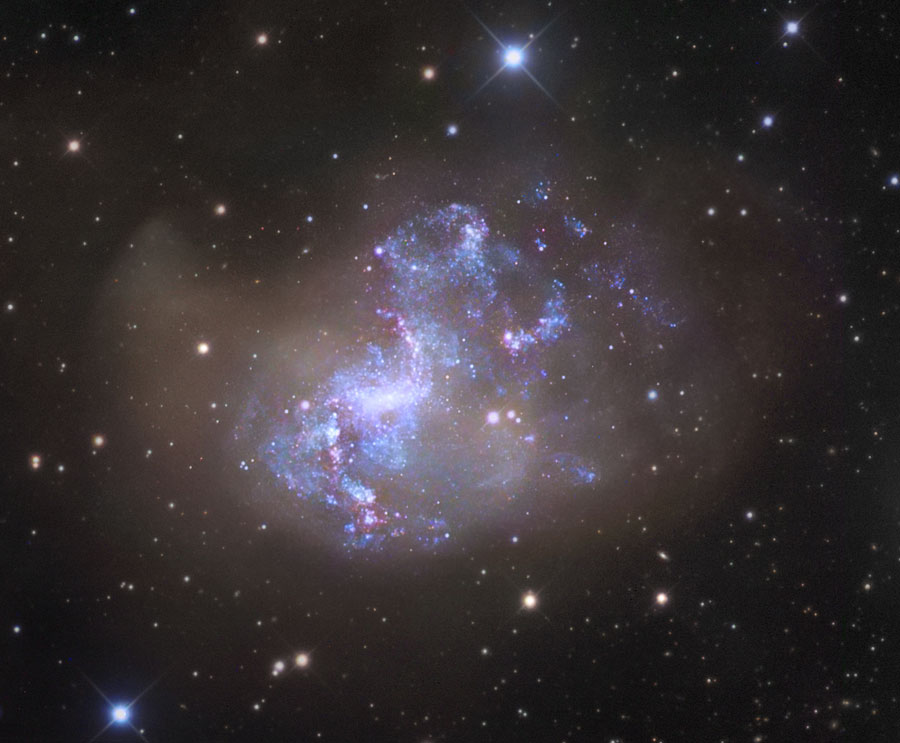 Die blau leuchtende Galaxie mit rosaroten Sternbildungsregionen hat zwar einen Zentralbalken, wirkt aber insgesamt sehr unregelmäßig, als hätte sie eine Kollision hinter sich.