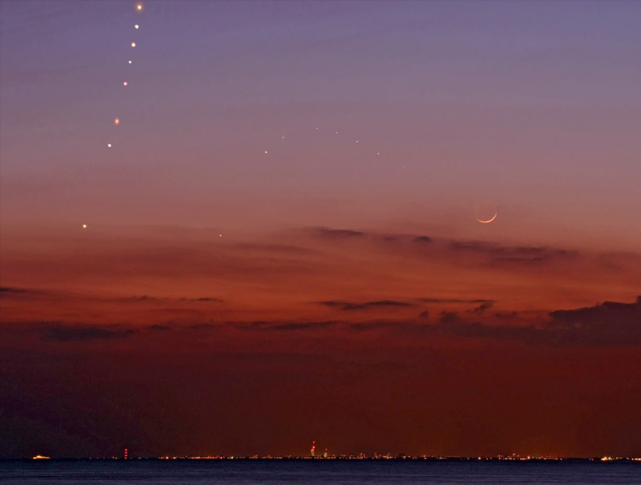 Links steigt der Planet Venus Abend für Abend höher aus der Dämmerung, rechts davon zieht der weniger helle Merkur einen Bogen, und ganz rechts leuchtet der Sichelmond in der rötlichen Abenddämmerung.