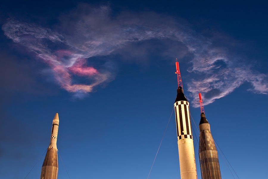 Drei Raketenspitzen ragen in einen glasklaren, blauen Himmel, darüber breitet sich eine dünne Abgasschwade aus, die teilweise rot beleuchtet ist.