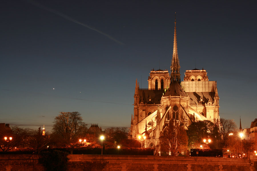Rechts im Bild steht die orangefarben beleuchtete Kathedrale Notre Dame in Paris. Links leuchten die Planeten Merkur und Venus.