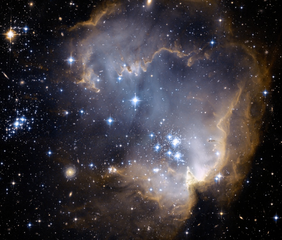 Im Bild sind einige Sternballungen, die an Juwelen erinnern. Dahinter leuchtet ein blaugrauer Nebel mit braunen, komprimierten Rändern.