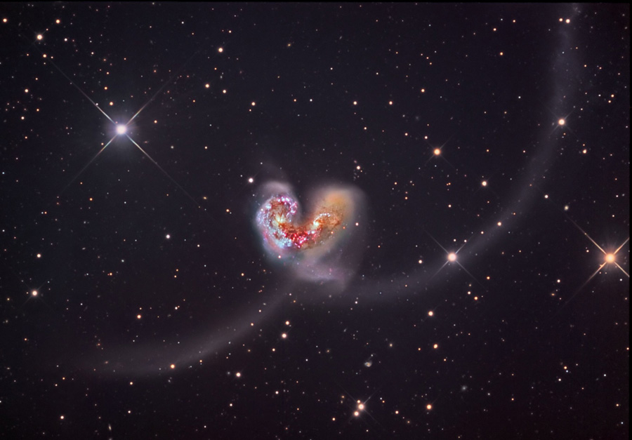 In der Mitte sind zwei Galaxien eng nebeneinander und verwickelt, nach links unten und rechts unten ziehen sich ausladende Gezeitenschweife aus Sternen.