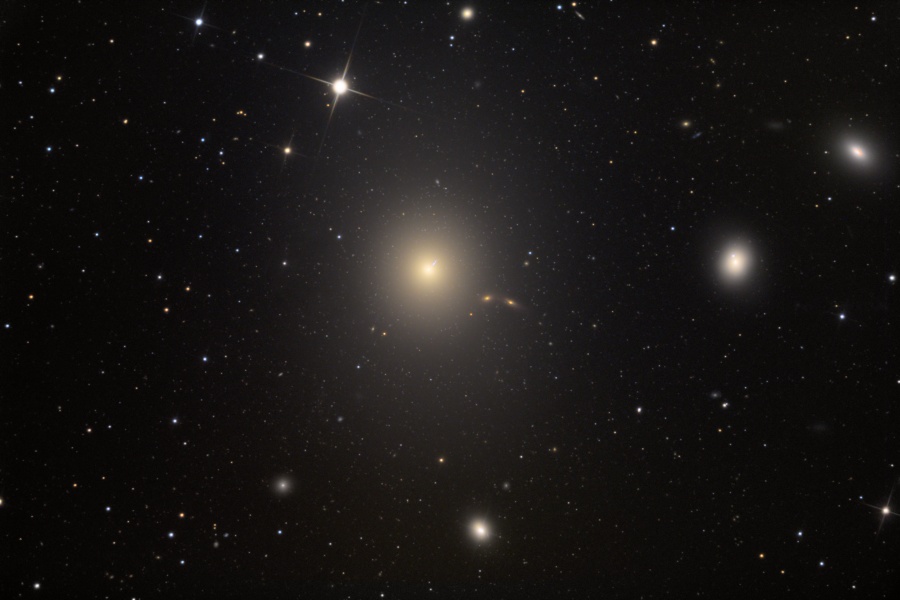 Im Bild sind mehrere elliptische Galaxien verteilt. Die Galaxie in der Bildmitte ist die größte, sie stößt einen Strahl aus.