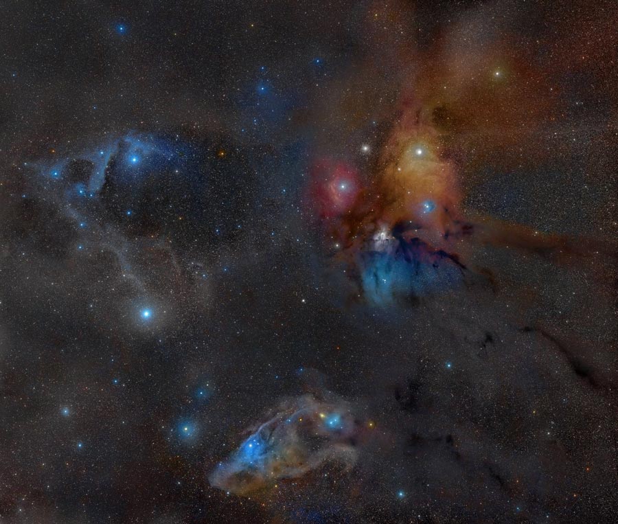 Die Wolken- und Sternenlandschaft zeigt unten den blauen Pferdekopfnebel, links einige blaue Reflexionsnebel und rechts oben eine bunte Sternenregion mit roten, blauen und gelben Nebeln sowie einem weißen Kugelsternhaufen.