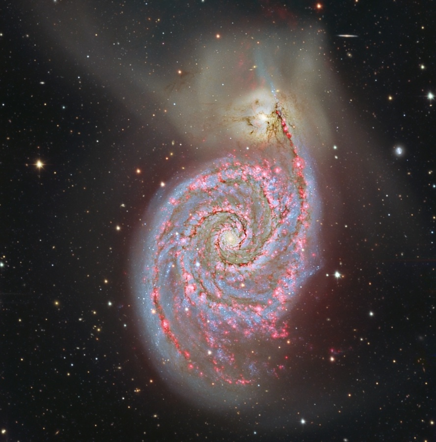 In der Bildmitte ist die Spiralgalaxie M51 mit vielen Sternbildungsregionen und einem ausgedehnten Nebel dargestellt, der sich nach oben hin ausbreitet.