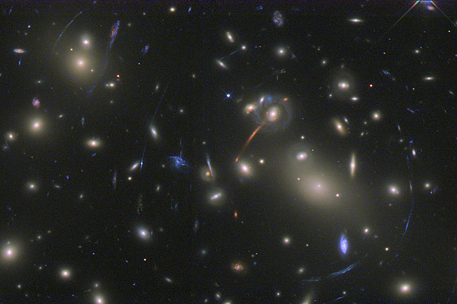 Im Bild sind viele Galaxien verteilt. Die zarten Bögen im Bild sind Bilder von Galaxien, die noch weiter entfernt sind.