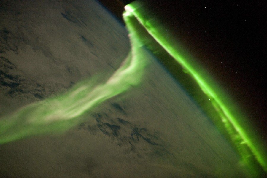 Über der dunklen Erde schlängelt sich ein langes, grünes Polarlicht.