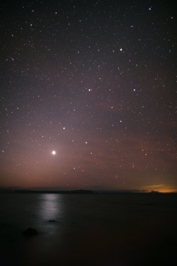 Über einem Gewässer leuchten die Planeten Venus, Mars und Saturn in den Sternbildern Löwe und Jungfrau.