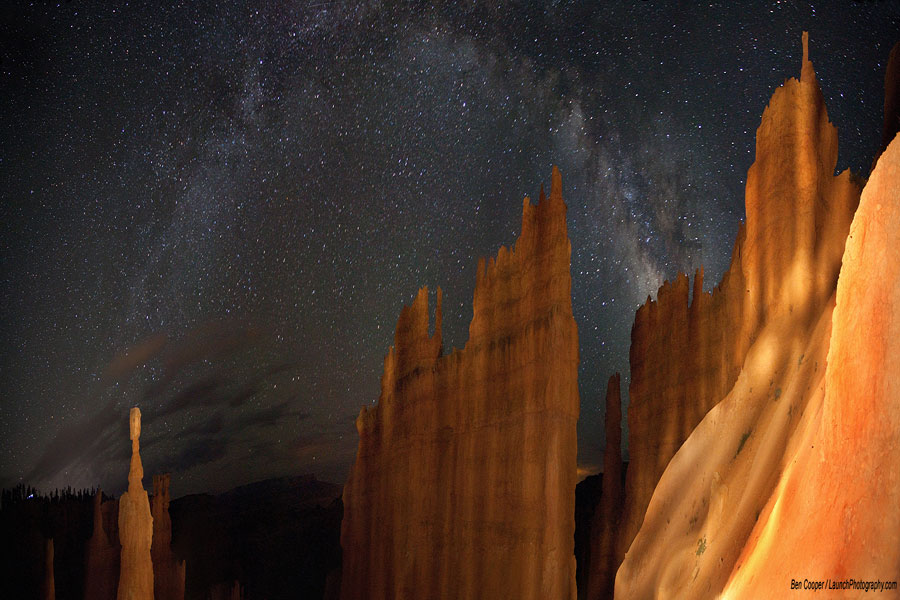 Über einer surreal wirkenden rötlichen Felslandschaft wölbt sich der Bogen der Milchstraße. Das Bild ist horizontal verkürzt.