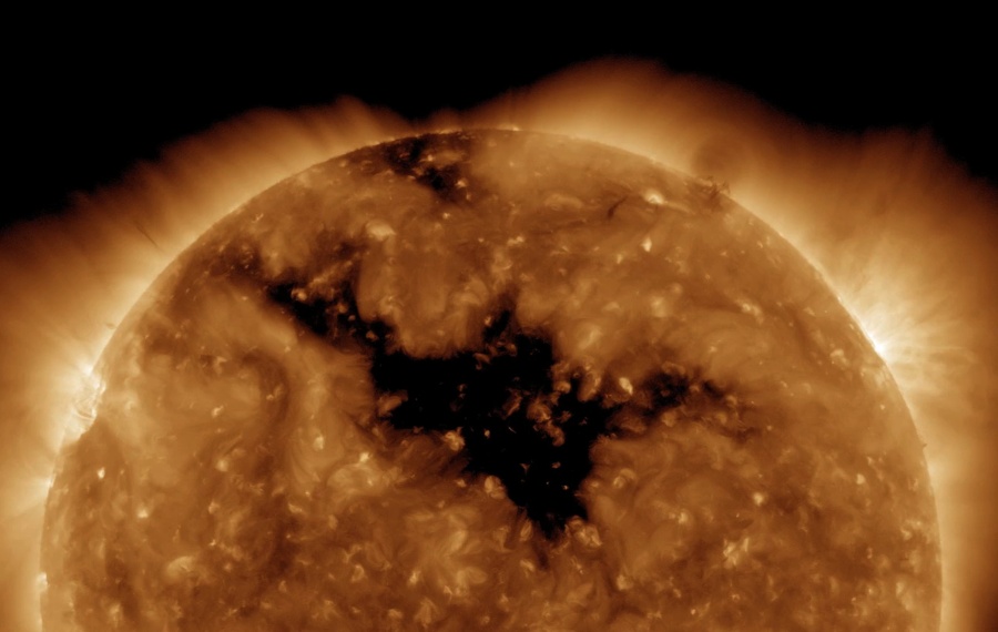 Im Bild ragt die Sonne auf, der untere Teil ist abgeschnitten. Die Oberfläche ist orange-braun gefleckt, in der Mitte ist ein riesiger dunkler Fleck mit einem Ausläufer nach links oben. Am Rand strahlt die Korona.