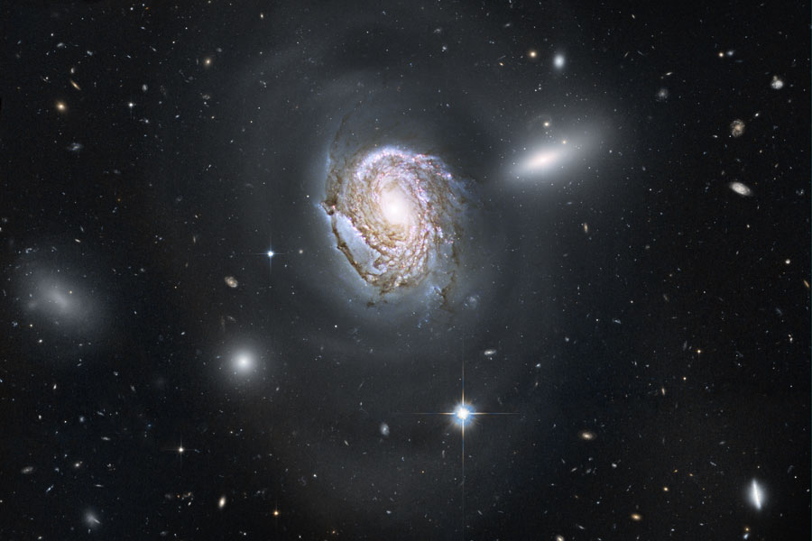 In der Mitte des Bildes ist eine große Spiralgalaxie, die von vielen weiteren Galaxien umgeben ist. Eine beschriftete Version ist darübergelegt, sie wird sichtbar, wenn man den Mauspfeil über das Bild schiebt.