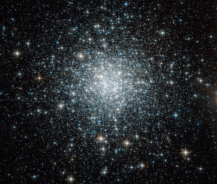Mitten im Bild prangt ein Kugelsternhaufen mit vielen Sternen, die in der Mitte sehr dicht gepackt sind.